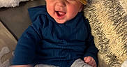 Bobby joined the competition — help win amazing prizes! baby, blue_sweater, cap, cheerful, child, couch, cozy, cute, furniture, happy, hat, indoor, infant, motion_blur, person, pillow, sitting, smile, soft_texture, wearing