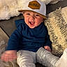 Bobby joined the competition — help win amazing prizes! baby, child, cap, hat, blue_sweater, couch, pillow, smile, happy, indoor, person, cute, infant, soft_texture, furniture, cozy, motion_blur, wearing, sitting, cheerful