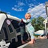toddler, child, pajamas, vehicle, reflection, blue_sky, clouds, house, trees, outdoor, sunlight, smiling, barefoot, curious, suburban, daytime, playing, person, family, happy