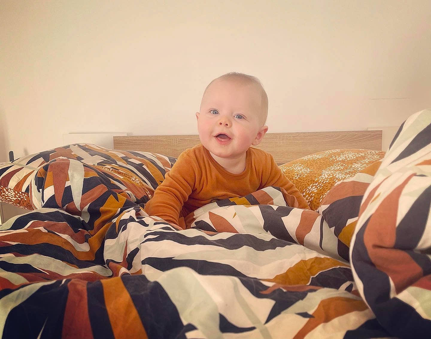 Naël a rejoint le concours — aidez-le/la à gagner de superbes lots ! baby, baby_toddler_clothing, bedding, bedroom, child, comfort, cool, flooring, fun, happy, linens, orange, pattern, person, room, sitting, sleeve, smile, t_shirt, toddler