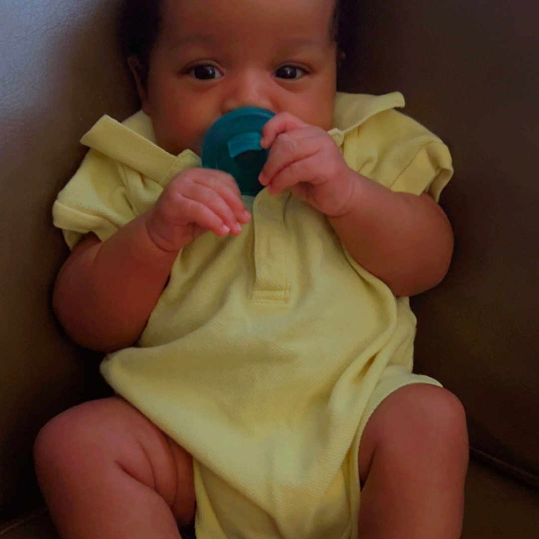 Blaze is registered to the contest to win money with this photo: baby, infant, pacifier, yellow_onesie, sitting, brown_leather_chair, cute, hands, feet, face, curious, indoor, child, young, portrait, comfort, clothing, skin, expression, person