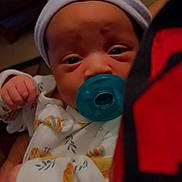 Blaze is registered to the contest to win money with this photo: baby, infant, pacifier, hat, onesie, clothing, face, hand, person, indoor, closeup, newborn, cute, sleepwear, child, portrait, soft_lighting, holding, warm_colors, young