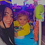 woman, baby, smile, indoor, activity_jumper, child, television, colorful, happy, person, long_hair, yellow_clothing, playtime, furniture, carpet, face, portrait, home, toy, living_room