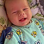 baby, infant, smiling, winking, onesie, cartoon_pattern, blanket, cute, happy, face, child, soft, cozy, lying_down, indoors, apparel, cheerful, adorable, expression, sleepwear