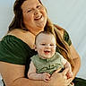 woman, baby, smiling, green_dress, green_outfit, happy, holding, portrait, indoor, light_background, family, mother, child, cute, skin, face, person, long_hair, sitting, together