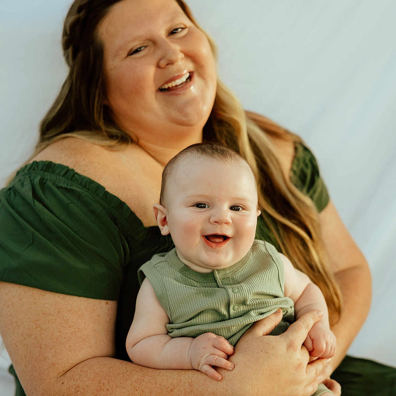 Caiden joined the competition — help win amazing prizes! woman, baby, smiling, green_dress, green_outfit, happy, holding, portrait, indoor, light_background, family, mother, child, cute, skin, face, person, long_hair, sitting, together