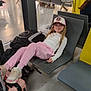 child, girl, airport, waiting_area, luggage, suitcase, hat, casual, pink_pants, sneakers, chair, public_space, people, shopping_area, floor, backpack, relaxed, indoor, waiting, travel