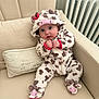 baby, cow_costume, onesie, hood, footwear, couch, cushion, radiator, indoor, child, cute, plush, seated, clothing, infant, hands, expression, face, adorable, soft