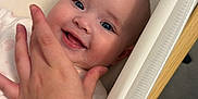 Heidi is registered to the contest to win money with this photo: baby, smiling, hand, bassinet, cozy, face, infant, comfort, child, cute, skin, person, happy, portrait, lying_down, fingers, blue_eyes, head, soft_light, indoors