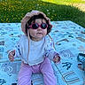 Charlie participe au concours pour gagner de l'argent avec cette photo : baby, child, sunglasses, hat, outdoor, grass, flowers, play_mat, pink_clothing, sitting, sunny, cute, infant, nature, greenery, casual, summer, young_child, headwear, toddler