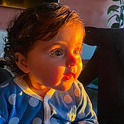 Charlie participe au concours pour gagner de l'argent avec cette photo : child, toddler, baby, face, curly_hair, blue_onesie, polka_dots, indoor, warm_light, sunlight, portrait, cute, expression, hands, person, young_child, cozy, home, soft_shadows, curiosity