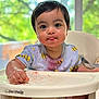 baby, child, face, messy, high_chair, food, red_stains, bee_pattern, shirt, hands, tongue_out, indoor, window, greenery, curious, cute, sitting, expression, young_child, portrait