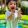 toddler, child, happy, smiling, clapping, wet_hands, striped_shirt, outdoor, pool, inflatable_pool, colorful, summer, play, water, garden, greenery, daylight, portrait, fun, joyful