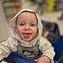 Elyo a rejoint le concours — aidez-le/la à gagner de superbes lots ! baby, child, shopping_cart, hood, clothing, face, tongue_out, smile, hand, store, blurred_background, infant, cute, person, indoor, panda, hooded_jacket, cart, playful, eyes