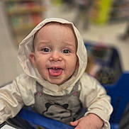 Elyo a rejoint le concours — aidez-le/la à gagner de superbes lots ! baby, child, shopping_cart, hood, clothing, face, tongue_out, smile, hand, store, blurred_background, infant, cute, person, indoor, panda, hooded_jacket, cart, playful, eyes