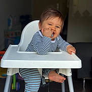 Livio participe au concours pour gagner de l'argent avec cette photo : baby, chewing, child, face, floor, foot, furniture, happy, high_chair, home, indoor, infant, legs, pacifier, person, playful, seat, smile, striped_pajamas, toy