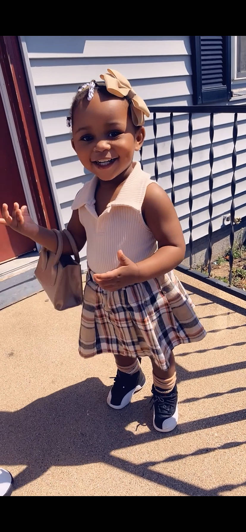 Jermahni is registered to the contest to win money with this photo: dress, eyewear, face, fence, fun, hand, happy, joy, knee, leg, leisure, pattern, person, plaid, shoe, smile, standing, street_fashion, tartan, toddler