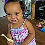 Kyomi is registered to the contest to win money with this photo: toddler, child, smiling, purple_bow, tie_dye, toothbrush, giraffe_shaped, indoor, wooden_floor, cabinet, fan, clothing, person, happy, cute, hair, hand, face, baby, playful