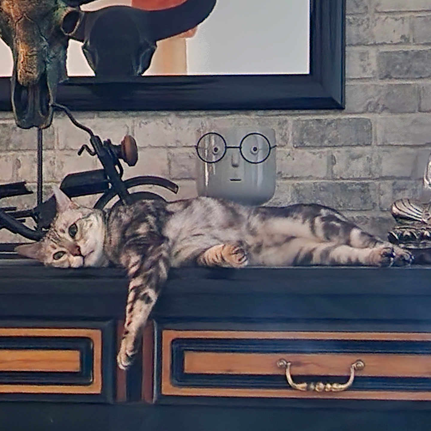 Louna participe au concours pour gagner de l'argent avec cette photo : artistic, brick_wall, buddha_statue, cat, decor, dormant, dresser, face_planter, feline, glasses, home, indoor, interior, motorcycle_sculpture, relaxed, resting, sprawled, tabby, vintage, wooden_furniture