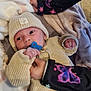 baby, infant, pacifier, knit_hat, sweater, blanket, hands, sibling_arm, butterfly_pattern, cozy, lying_down, indoors, tile_floor, soft_texture, close_up, portrait, neutral_expression, button, holding, newborn