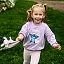 child, girl, pigtails, sweatshirt, stitch, toy, grass, outdoor, playful, running, greenery, leggings, smile, happy, daylight, casual_clothing, cute, young_child, nature, fun