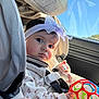 baby, car_seat, headband, toy, car_interior, child, window, sunlight, seatbelt, clothing, face, hand, expression, infant, safety, seat, colorful, young_child, portrait, indoor