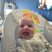 Ryker joined the competition — help win amazing prizes! baby, smiling, infant, baby_seat, onesie, animal_print, indoor, home, television, shelf, furniture, child, happy, cute, face, person, seat, cozy, pattern, room