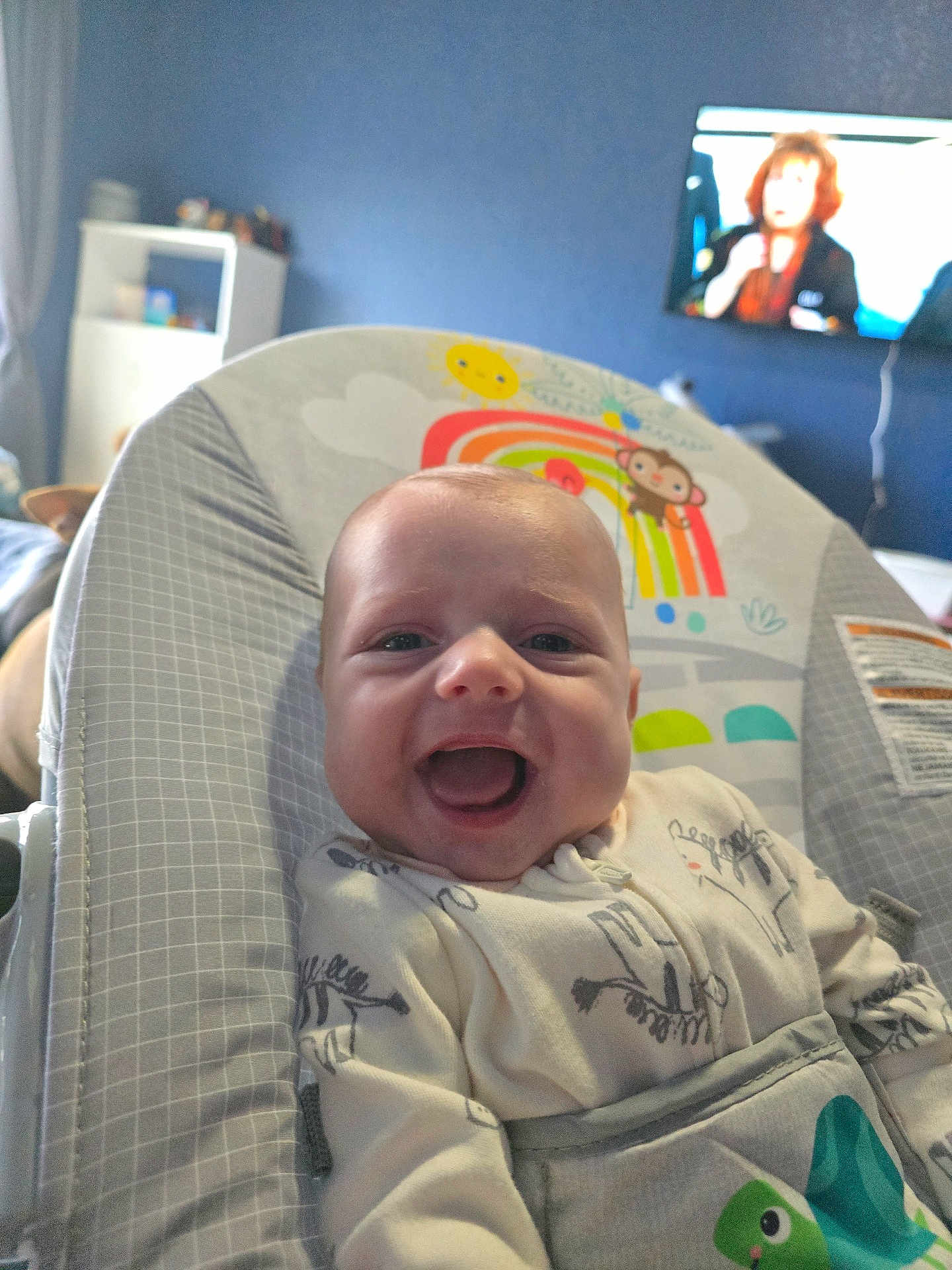 Ryker joined the competition — help win amazing prizes! baby, smiling, infant, baby_seat, onesie, animal_print, indoor, home, television, shelf, furniture, child, happy, cute, face, person, seat, cozy, pattern, room