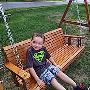 Adrian is registered to the contest to win money with this photo: bench, boy, camouflage, casual, chain, child, daylight, grass, outdoor, playground, relaxed, shorts, smiling, sneakers, suburban, summer, superman_logo, swing, tshirt, wooden_swing