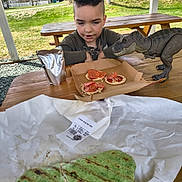 Adrian joined the competition — help win amazing prizes! child, toy_dinosaur, pepperoni, cracker, picnic_table, outdoor, grass, house, drink_pouch, wood, paper_wrapper, food, snack, curly_hair, daylight, bench, playful, greenery, casual, portrait