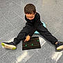 activity, black_board, black_pants, black_shirt, boy, casual_clothing, child, education, floor, focused, golden_lines, green_circles, indoor, learning, person, pointing, sitting, sneakers, tile_floor, young