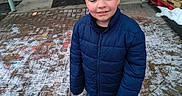 Adrian is registered to the contest to win money with this photo: blue_jacket, boy, brick_pavement, building_entrance, casual, child, closed_eyes, concrete, door, green_door, jacket, outdoor, person, sidewalk, smiling, sneakers, snow, winter_clothing, wooden_pallets, young
