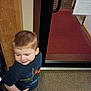 Benjamin is registered to the contest to win money with this photo: child, boy, indoor, carpet, door, mat, wood_paneling, brick_wall, sneakers, tshirt, shorts, standing, motion_blur, smile, young_child, person, casual_clothing, red, blue, playful