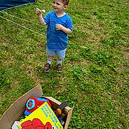 Benjamin is registered to the contest to win money with this photo: child, boy, grass, outdoor, tent, toys, bubble_wand, bubble_bottle, cardboard_box, elmo_book, clothing, shoes, shorts, blue_shirt, greenery, play, fun, daylight, smile, young