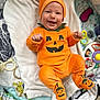 Sohan a rejoint le concours — aidez-le/la à gagner de superbes lots ! baby, infant, orange_outfit, pumpkin_costume, smiling, happy, blanket, toy, colorful, cute, festive, lying_down, headwear, footed_pajamas, indoors, child, face, patterned_background, playmat, cozy