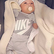 Novel is registered to the contest to win money with this photo: baby, blanket, pacifier, hat, mittens, socks, clothing, nike_logo, infant, gray_outfit, cozy, cute, lying_down, fabric, soft_texture, indoor, newborn, child, person, portrait