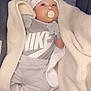 baby, blanket, pacifier, hat, mittens, socks, clothing, nike_logo, infant, gray_outfit, cozy, cute, lying_down, fabric, soft_texture, indoor, newborn, child, person, portrait