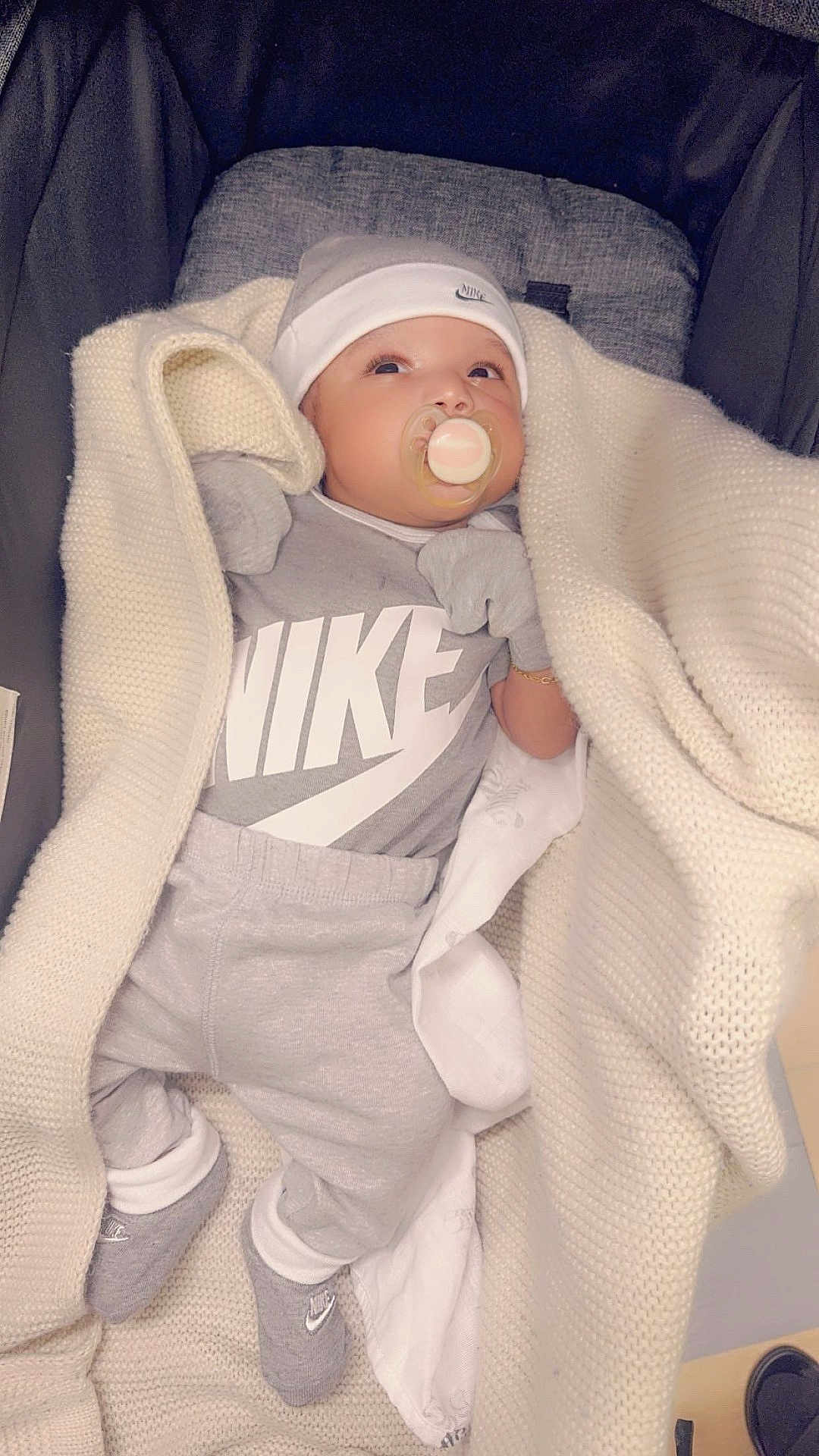 Novel is registered to the contest to win money with this photo: baby, blanket, pacifier, hat, mittens, socks, clothing, nike_logo, infant, gray_outfit, cozy, cute, lying_down, fabric, soft_texture, indoor, newborn, child, person, portrait