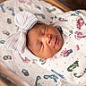 newborn, baby, sleeping, blanket, headband, bow, hospital, bassinet, footprint_pattern, wrapped, infant, peaceful, soft_lighting, cute, portrait, child, closeup, indoors, resting, sleep