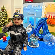 Matthias-Gabriel joined the competition — help win amazing prizes! child, police_costume, birthday_party, cake, balloons, thumbs_up, table, blue_tablecloth, christmas_tree, indoor, celebration, festive, party_decorations, smiling, portrait, young_child, hat, costume, holiday, fun