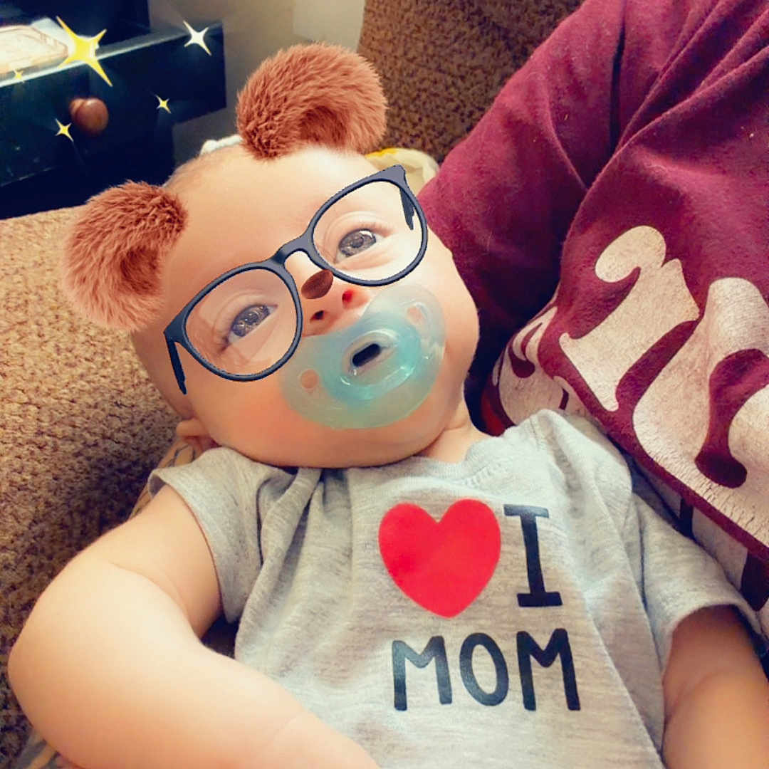 Kinslee joined the competition — help win amazing prizes! baby, onesie, pacifier, glasses_filter, bear_ears_filter, couch, brown_couch, arm, hand, infant, child, indoor, person, cute, filter_effect, smile, relaxing, love_mom, casual_clothing, portrait
