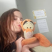 Julia participe au concours pour gagner de l'argent avec cette photo : child, girl, plush_toy, tigger, stuffed_animal, hugging, indoor, door, paper, casual, long_hair, black_shirt, expression, puckered_lips, hand, face, toy, childhood, cute, soft_toy