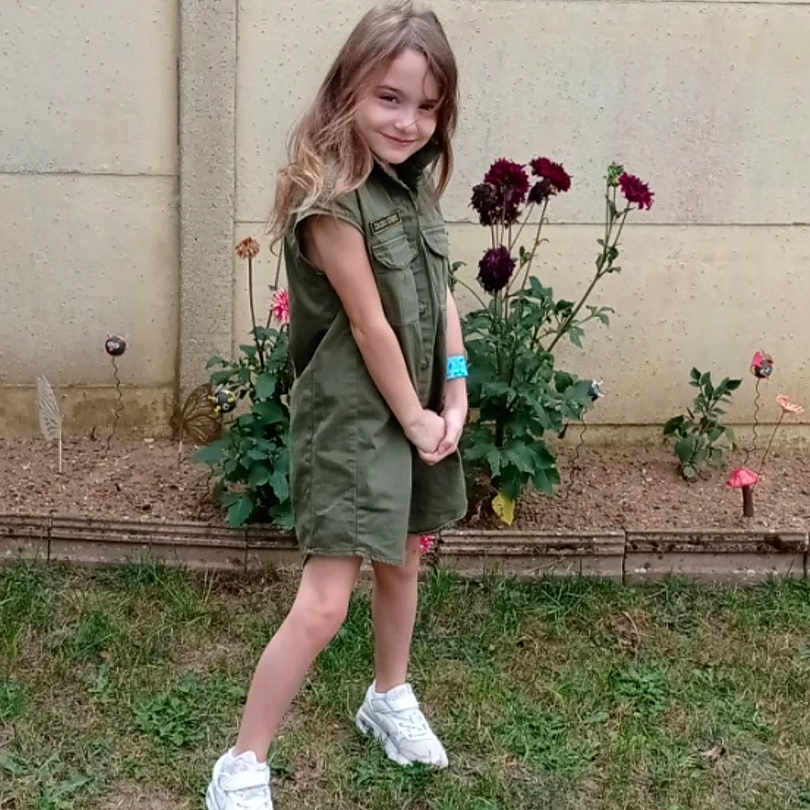 Julia participe au concours pour gagner de l'argent avec cette photo : background, casual, child, feet, flowers, garden, girl, grass, green_dress, happy, nature, outdoor, plants, playful_pose, portrait, smile, wall, white_sneakers, wristband, young