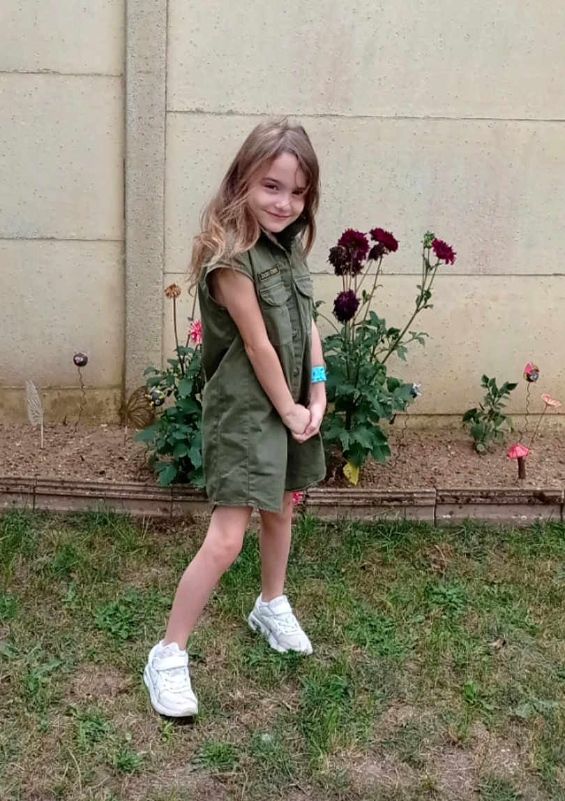 Julia participe au concours pour gagner de l'argent avec cette photo : child, girl, green_dress, white_sneakers, garden, flowers, grass, playful_pose, smile, wristband, outdoor, plants, nature, young, portrait, casual, wall, background, happy, feet
