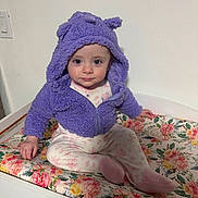 Samantha joined the competition — help win amazing prizes! baby, child, purple_jacket, hood, floral_pattern, changing_pad, sitting, indoor, white_wall, cute, blue_eyes, smile, clothing, person, infant, footed_pajamas, apparel, baby_girl, soft_texture, portrait