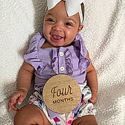 Halo joined the competition — help win amazing prizes! baby, infant, child, smiling, white_bow, headband, purple_outfit, ruffles, floral_bloomers, milestone_disc, four_months, blanket, chubby_legs, sitting, happy, portrait, indoor, hand, button, closeup