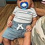 Josiah joined the competition — help win amazing prizes! baby, pacifier, infant, child, sitting, indoor, person, clothing, shorts, socks, hand, flooring, tattoo, adult, jeans, chair, wood_floor, blue, white, camouflage