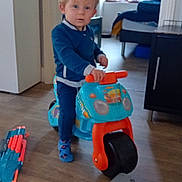 Noa a rejoint le concours — aidez-le/la à gagner de superbes lots ! toddler, child, indoor, toy, plastic_toy, ride_on_toy, blue_clothing, socks, wooden_floor, window, furniture, cabinet, floor_toys, curious, standing, person, home, natural_light, room, playful