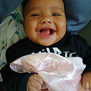 Kayvon is registered to the contest to win money with this photo: baby, smiling, blanket, hand, face, pillow, clothing, child, happy, indoors, cute, infant, portrait, skin, holding, fabric, person, cozy, toddler, bed