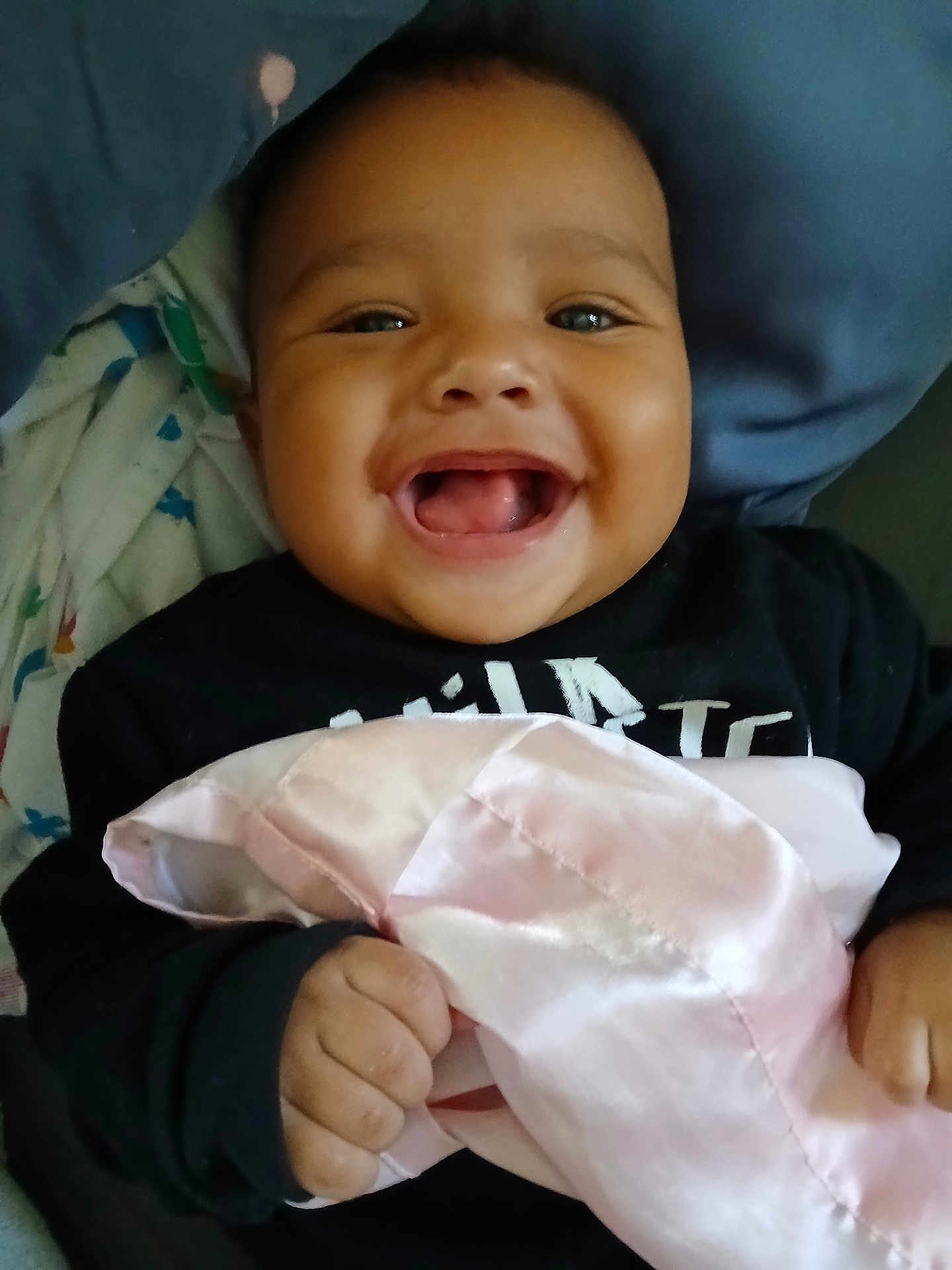 Kayvon is registered to the contest to win money with this photo: baby, smiling, blanket, hand, face, pillow, clothing, child, happy, indoors, cute, infant, portrait, skin, holding, fabric, person, cozy, toddler, bed